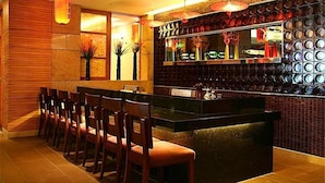 A bar area with a long counter, several chairs, and decorative elements like vases and a wall of circular mirrors. - Zhongshan International Hotel (Zhongshan)