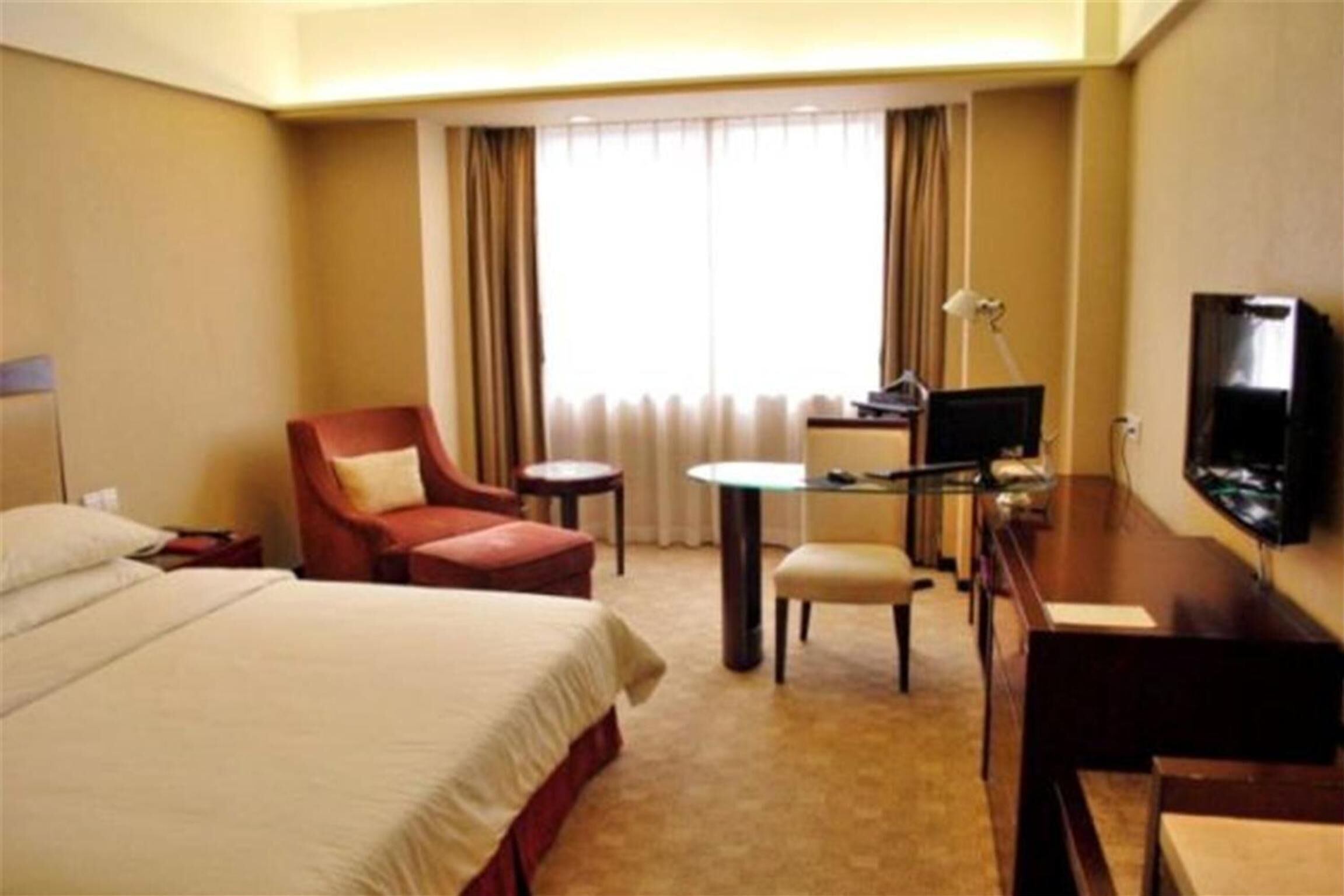 Une chambre d’hôtel équipée d’un lit, d’un bureau, d’une chaise, d’une télévision et d’une fenêtre avec des rideaux.