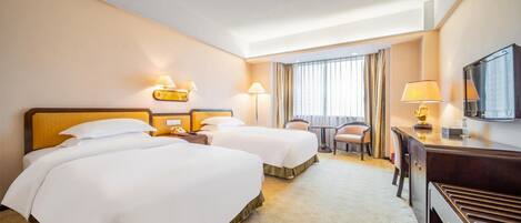 A hotel room with two beds, a desk, a chair, and a television.
