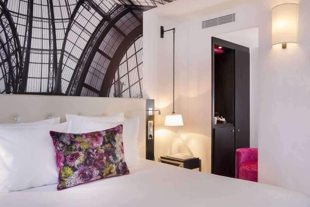 A hotel room with a large bed, a nightstand, a lamp, a wardrobe, and a skylight.