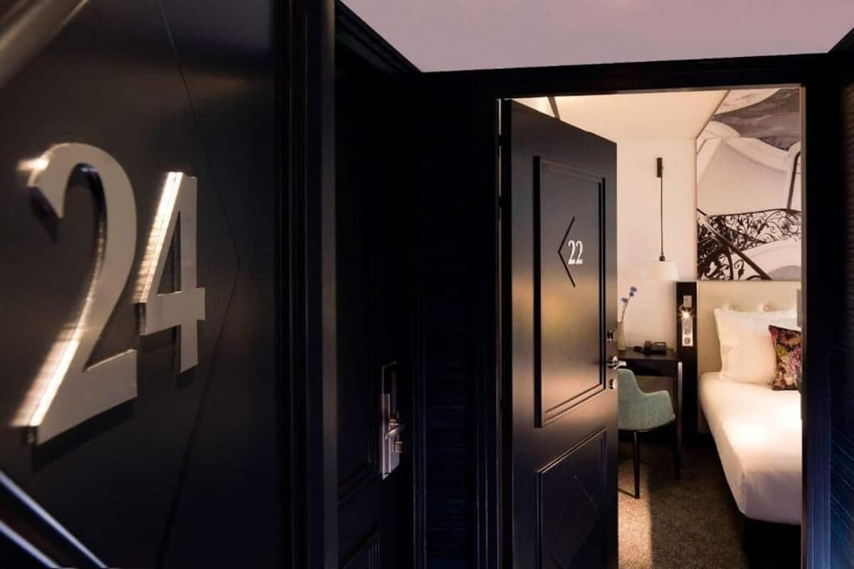 A hotel room with a bed, a desk, a chair, and a door with the number 24.