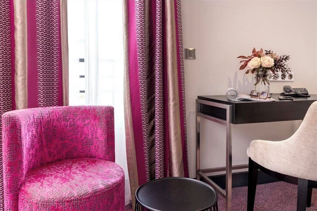 Una habitación con un sofá estampado rosa, una silla blanca, un escritorio con un florero y una silla negra.