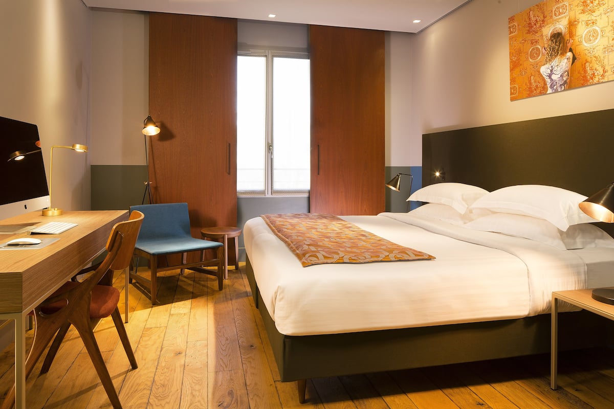 Habitación de hotel con cama, escritorio, silla y un cuadro en la pared.