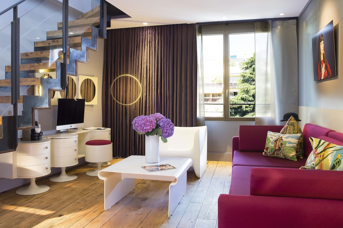 Una sala de estar moderna con una escalera, un televisor de pantalla plana, una mesa de centro blanca, un sofá rojo y un ventanal con vistas a zonas verdes.