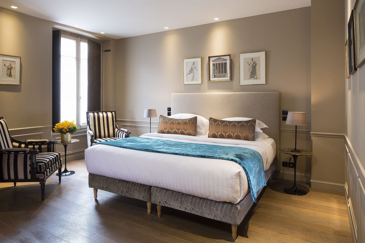 Un dormitorio moderno con una cama grande, dos mesitas de noche, una silla y una obra de arte en la pared.
