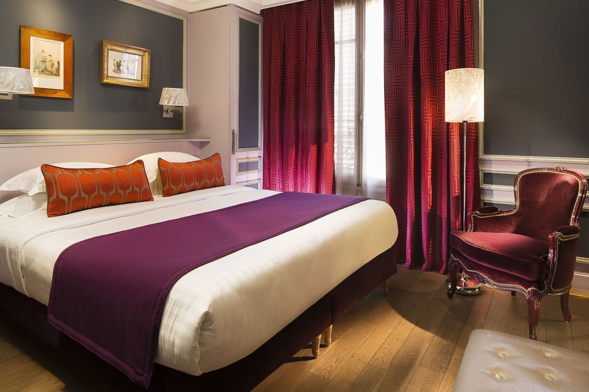 Una habitación de hotel con una cama grande, una silla roja y dos cuadros en la pared.