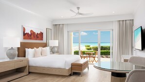 A modern hotel room with a large bed, a glass table, and a view of the beach. - Alexandra Resort - All-Inclusive (Providenciales)