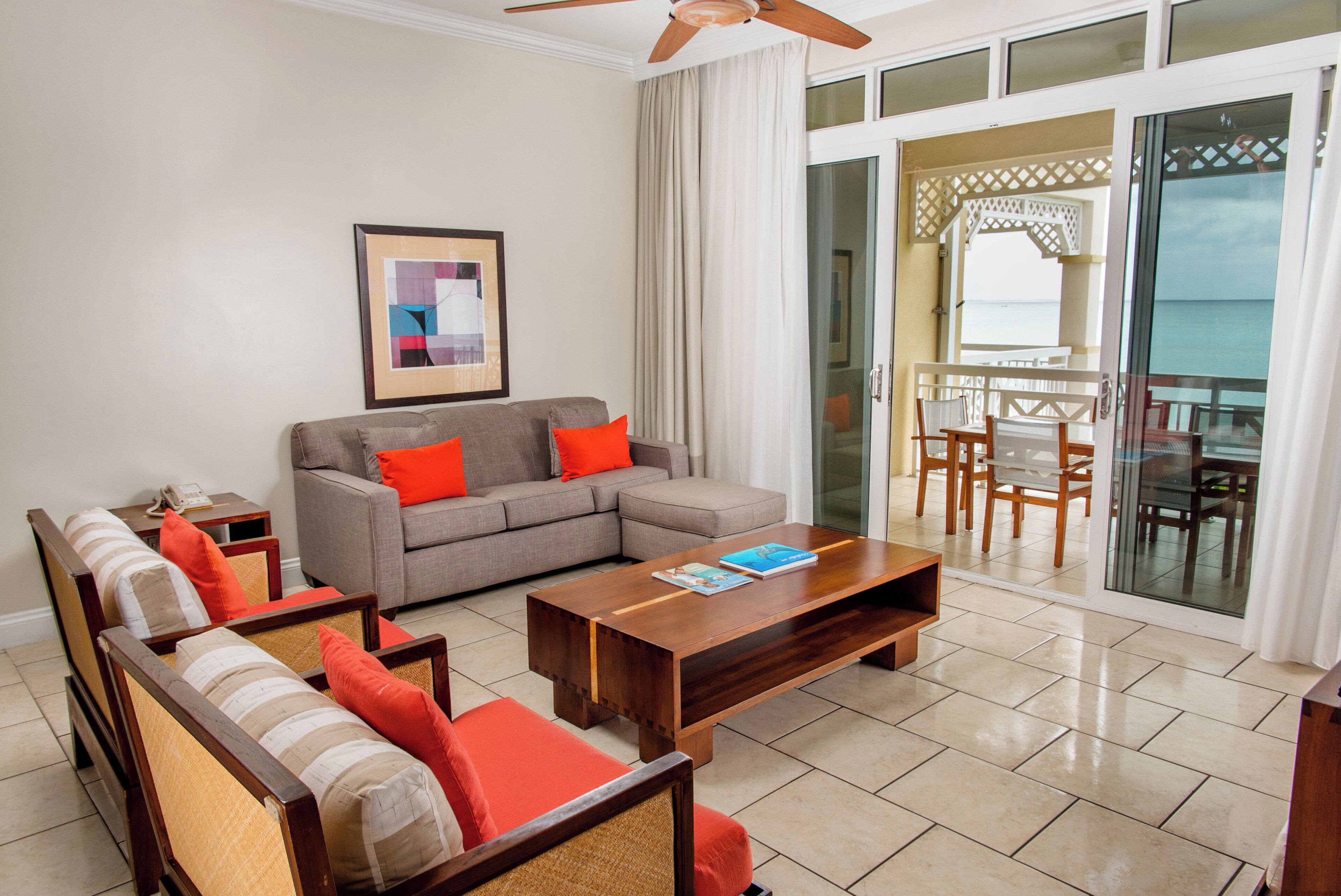 A living room with a sofa, armchairs, a coffee table, and a balcony with a view of the sea.