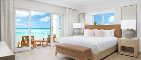 A spacious bedroom with a large bed, a wooden bench, a nightstand, and a view of the ocean.