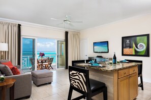 A hotel room with a balcony, a dining area, a TV, and a kitchen counter.