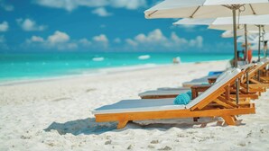 A row of wooden lounge chairs with white umbrellas on a sandy beach. - Alexandra Resort - All-Inclusive (Providenciales)