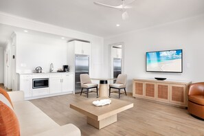 A modern kitchen with white cabinetry, a dining area with a round table, and a television on the wall.