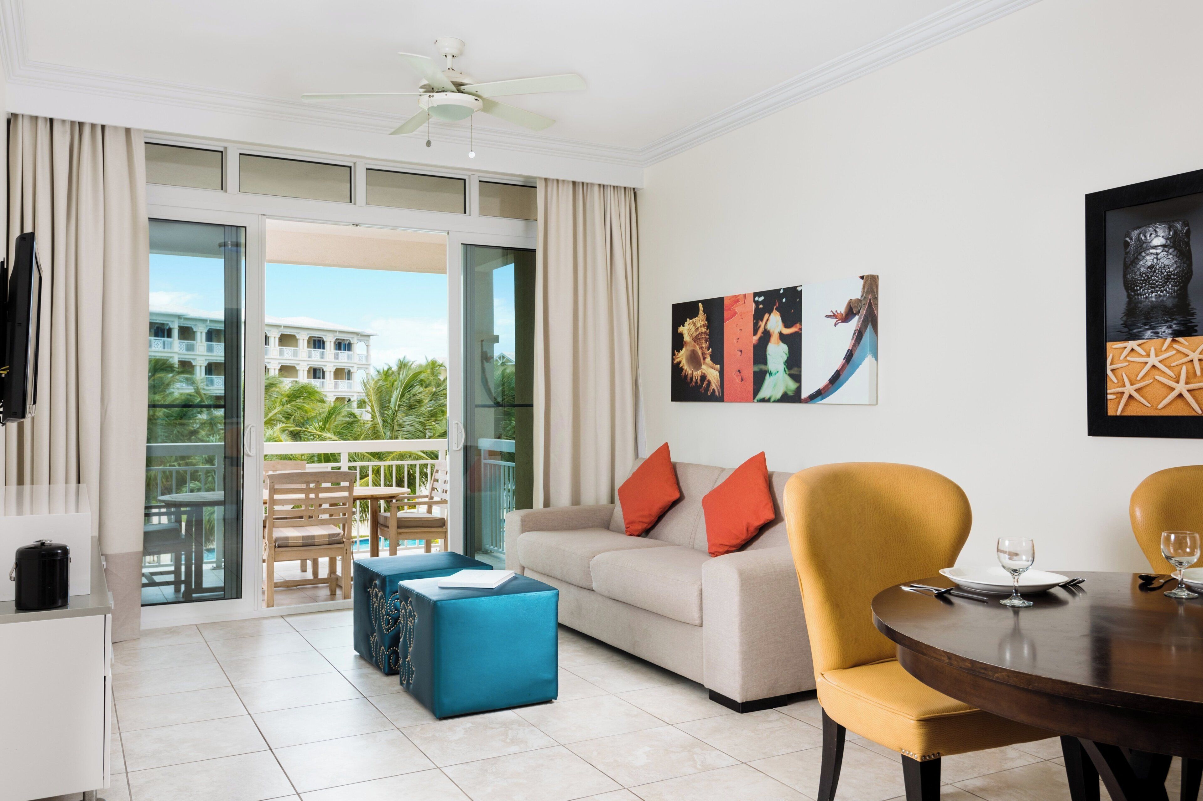 Una habitación de hotel moderna con balcón, sofá, mesa de comedor y obras de arte en las paredes.