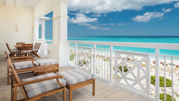 A wooden deck with lounge chairs and a table, overlooking a beach with clear turquoise water and a white railing. - Alexandra Resort - All-Inclusive (Providenciales)