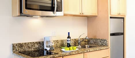 A kitchen with wooden cabinets, a stainless steel microwave, a coffee maker, and a sink.