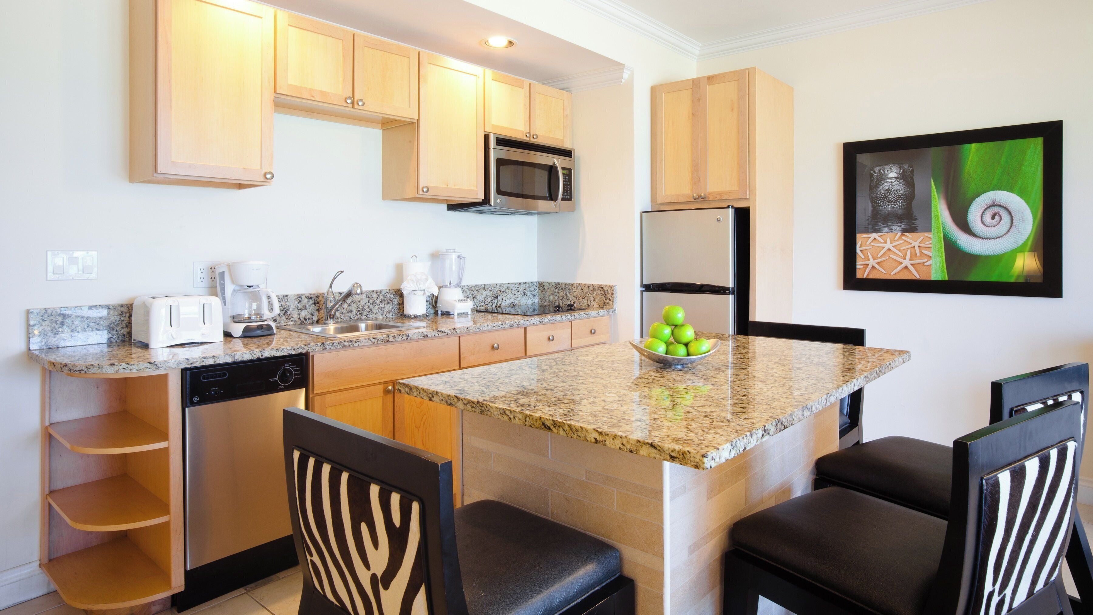 A kitchen with granite countertops, wooden cabinets, a microwave, a coffee maker, and a bowl of green apples on the island.