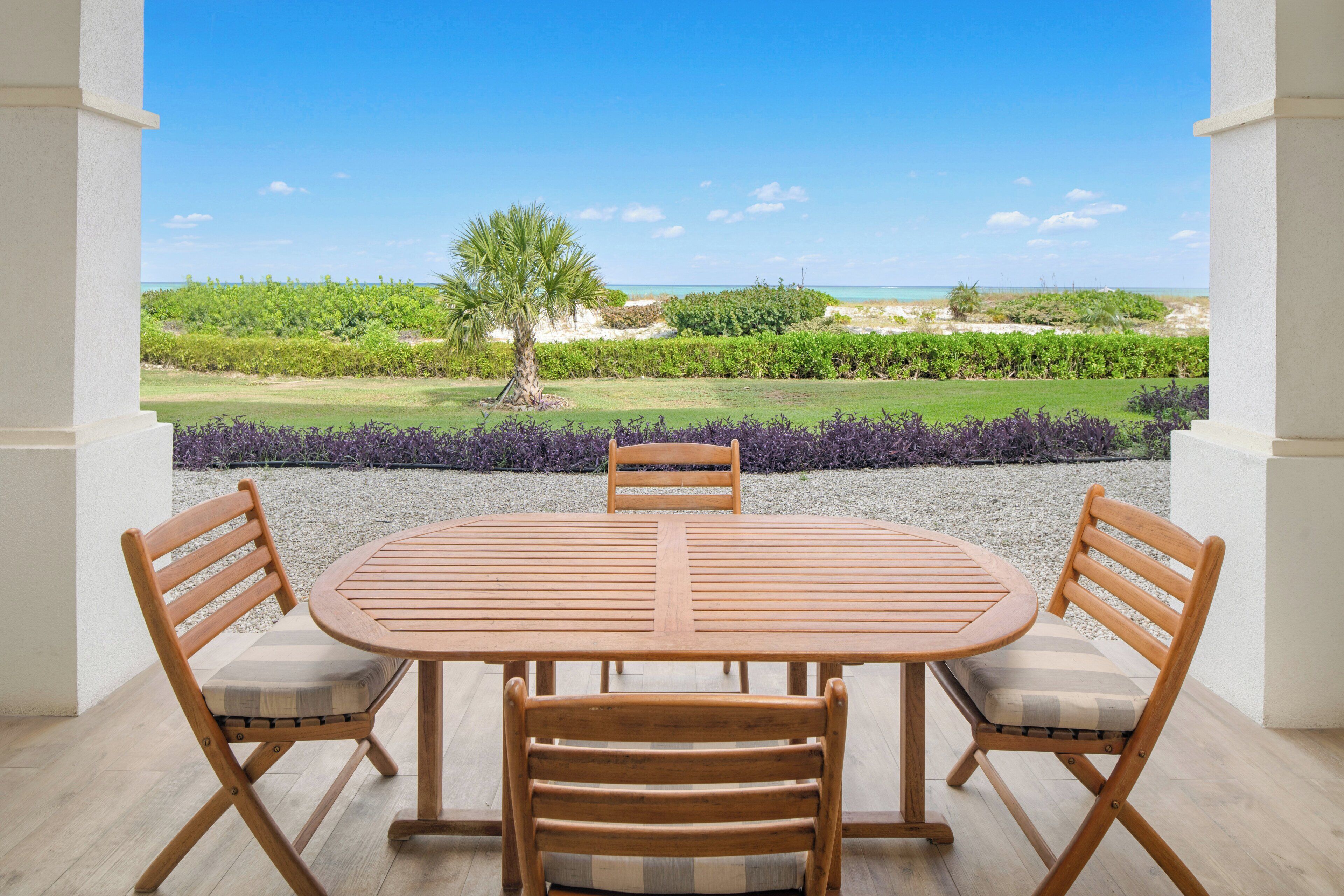 A wooden table with four chairs, a view of a beach, and a palm tree.