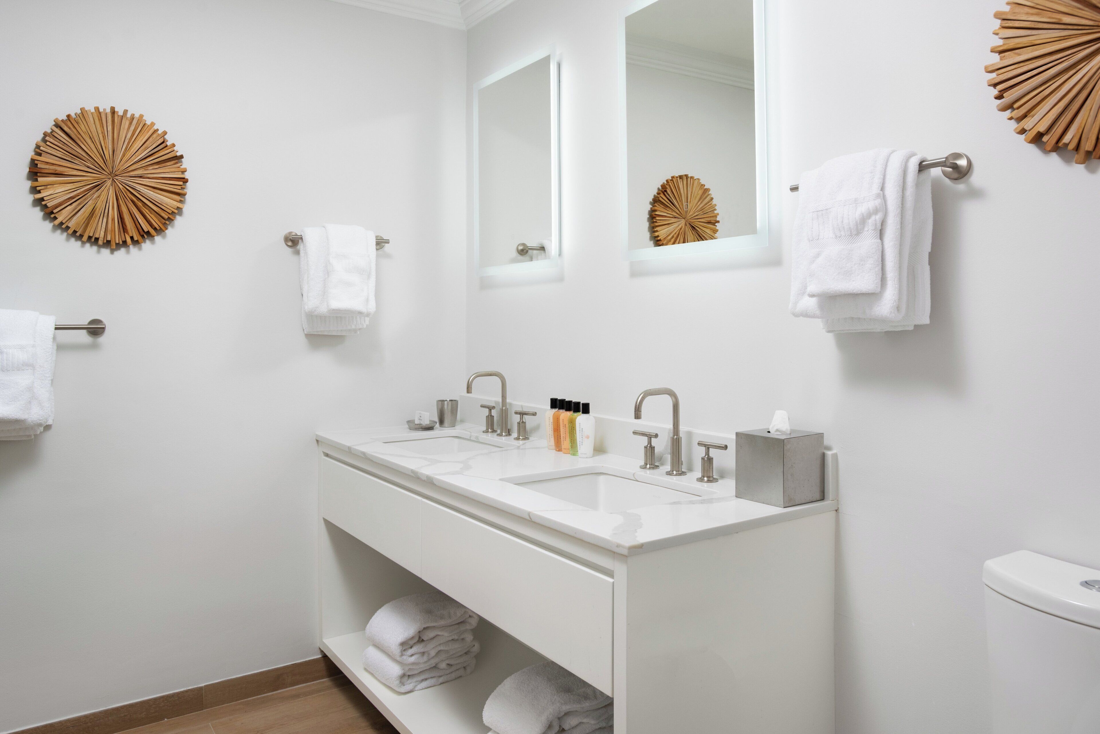 Un baño moderno con tocador doble lavamanos, inodoro y dos espejos montados en la pared.