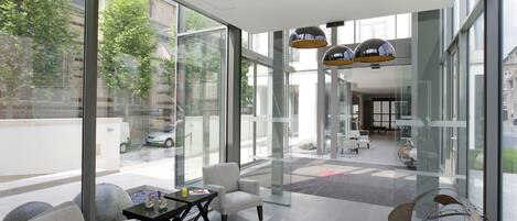 Um lobby moderno com grandes portas de vidro, área de estar com mesa e uma escultura abstrata singular.