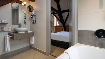 Een moderne badkamer met een groot bad, een wastafel met spiegel en een haardroger aan de muur.