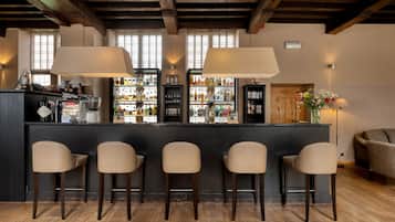 A bar area with four stools, wooden flooring, and a bar stocked with various bottles.