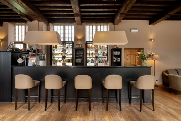 A bar area with four stools, wooden flooring, and a bar stocked with various bottles. - Martin's Klooster (Leuven)