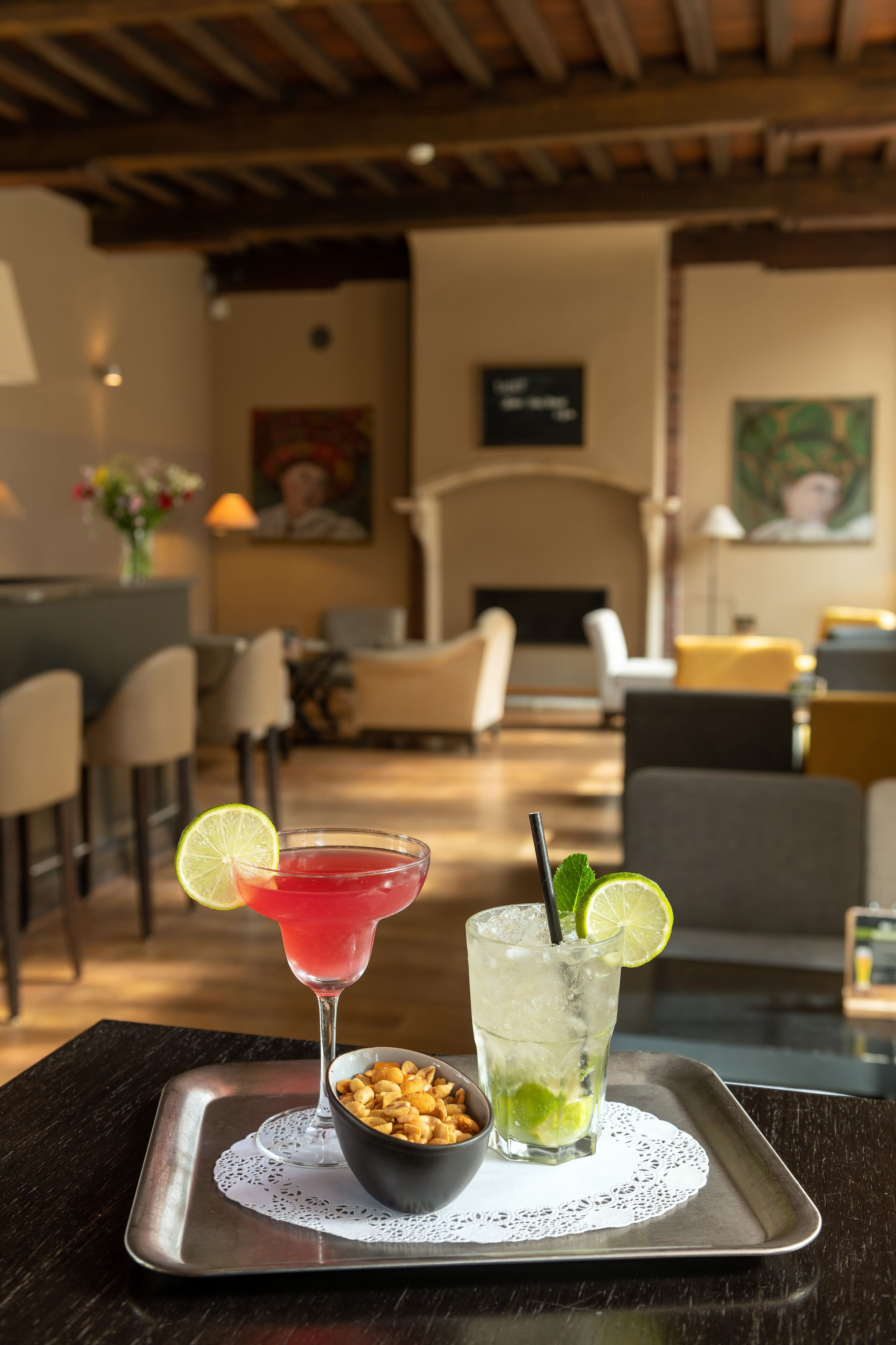 A bar area with a tray holding two drinks, one red and one green, and a bowl of nuts.