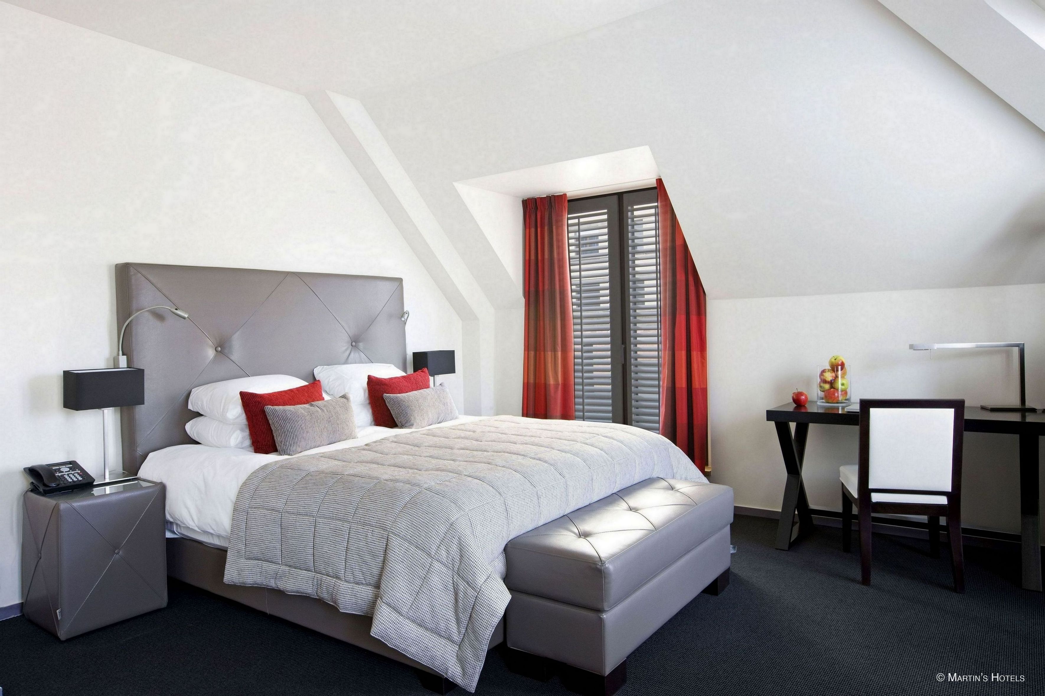 A modern hotel room with a large bed, a desk, and a chair.