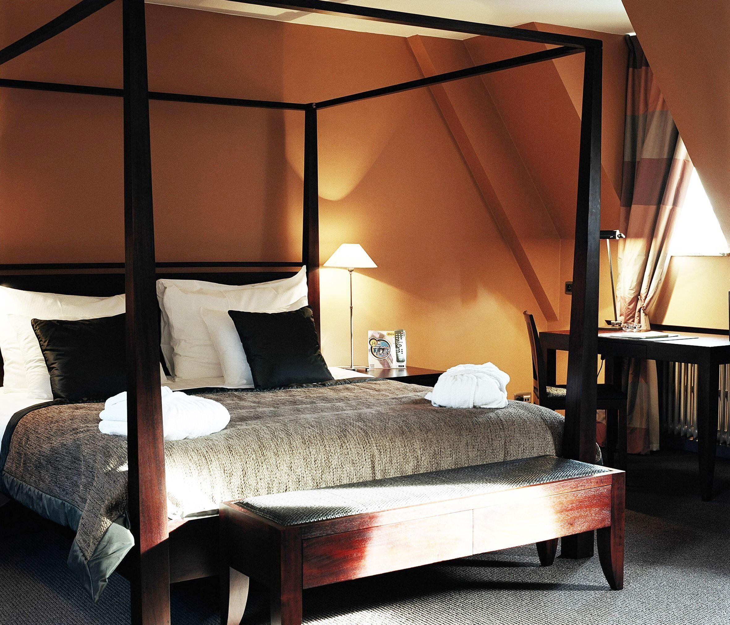 A four-poster bed with a wooden frame, a bedside table with a lamp, and a chair.