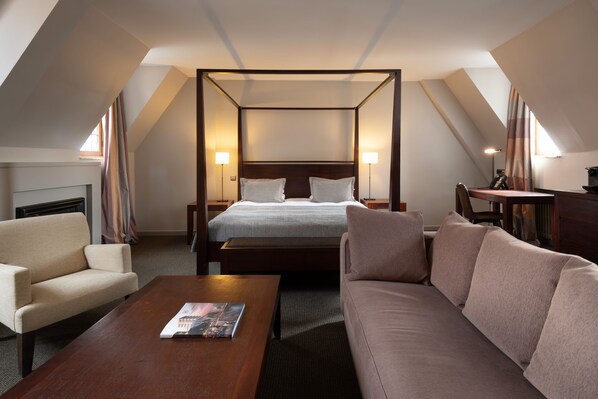 A modern hotel room with a four-poster bed, a sofa, a coffee table, and a desk with a lamp. - Martin's Klooster (Leuven)
