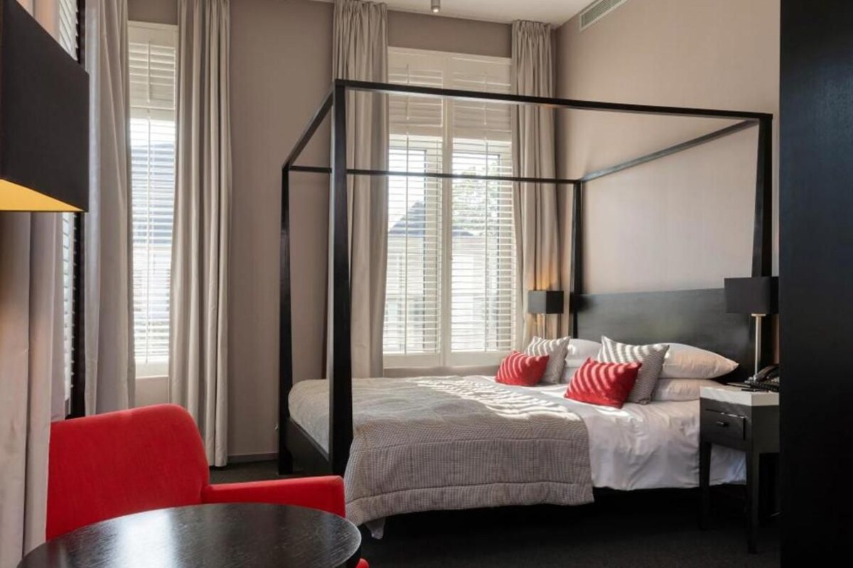 Quarto de hotel com cama de dossel, escrivaninha, cadeira e mesa pequena.