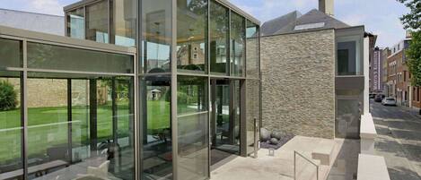 A modern building with large glass windows, a stone facade, and a paved outdoor area with seating.