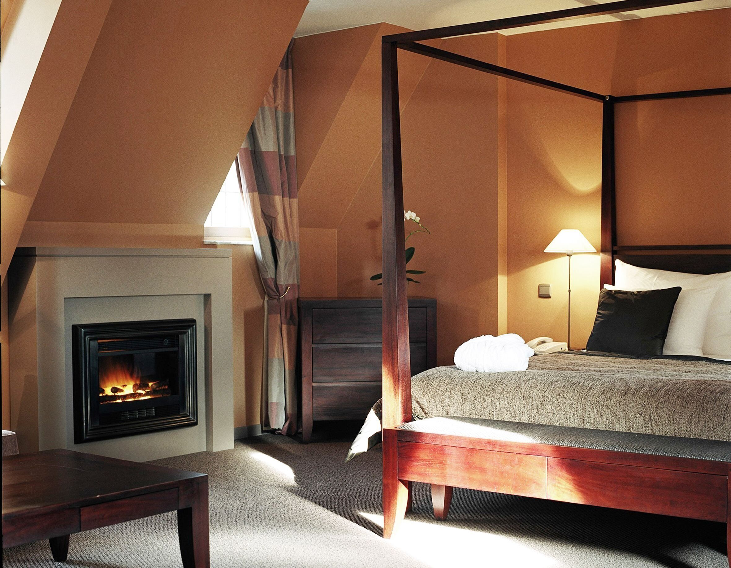 Une chambre à coucher avec un lit à baldaquin, une table de chevet, une lampe, un téléphone et une cheminée.