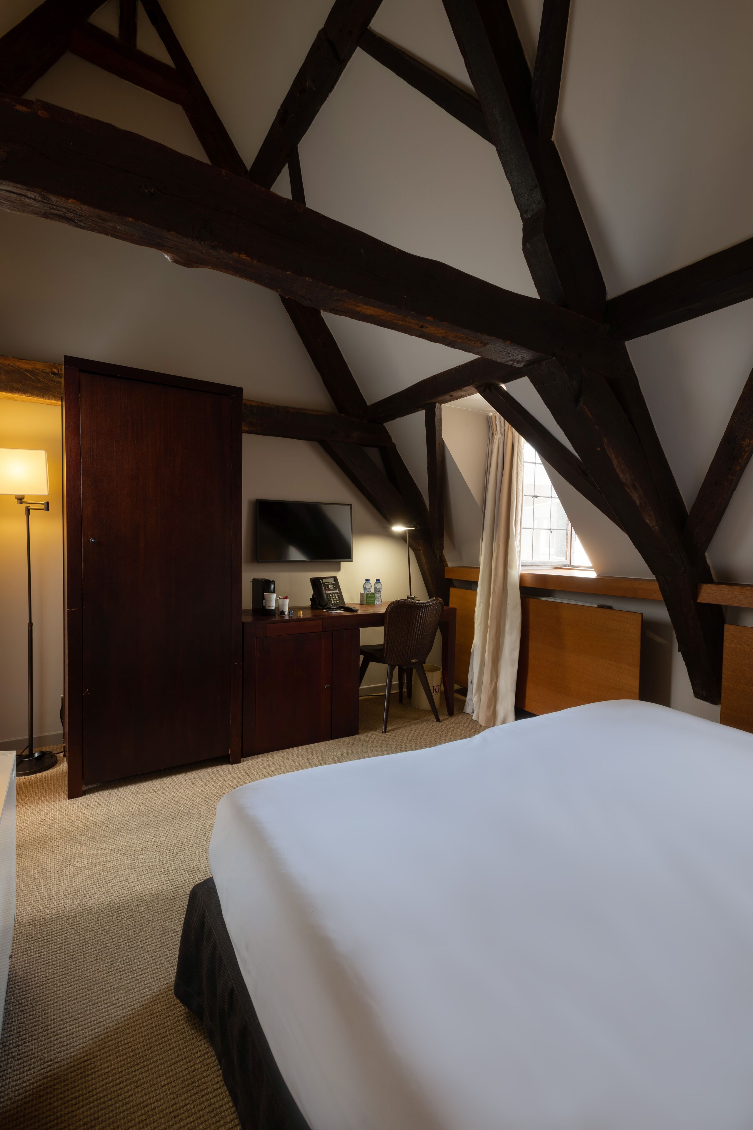 A bedroom with a large bed, a desk with a chair, a television, and a wardrobe.