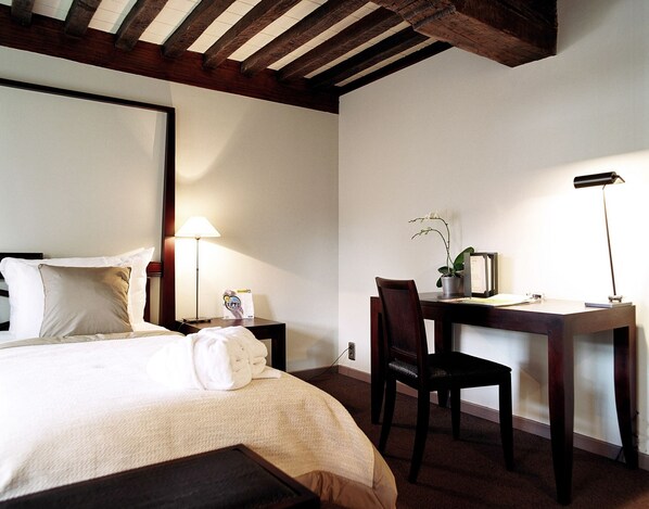 A hotel room with a bed, a desk, a chair, a lamp, and a potted plant. - Martin's Klooster (Leuven)