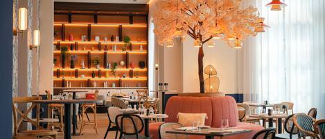 Un restaurante con un árbol central, mesas, sillas y una zona de bar con estanterías.