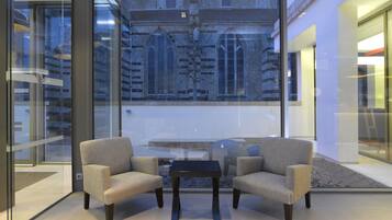 Un interior moderno con dos sillones y una mesita, un ventanal con vistas a un edificio histórico, y un separador de vidrio.