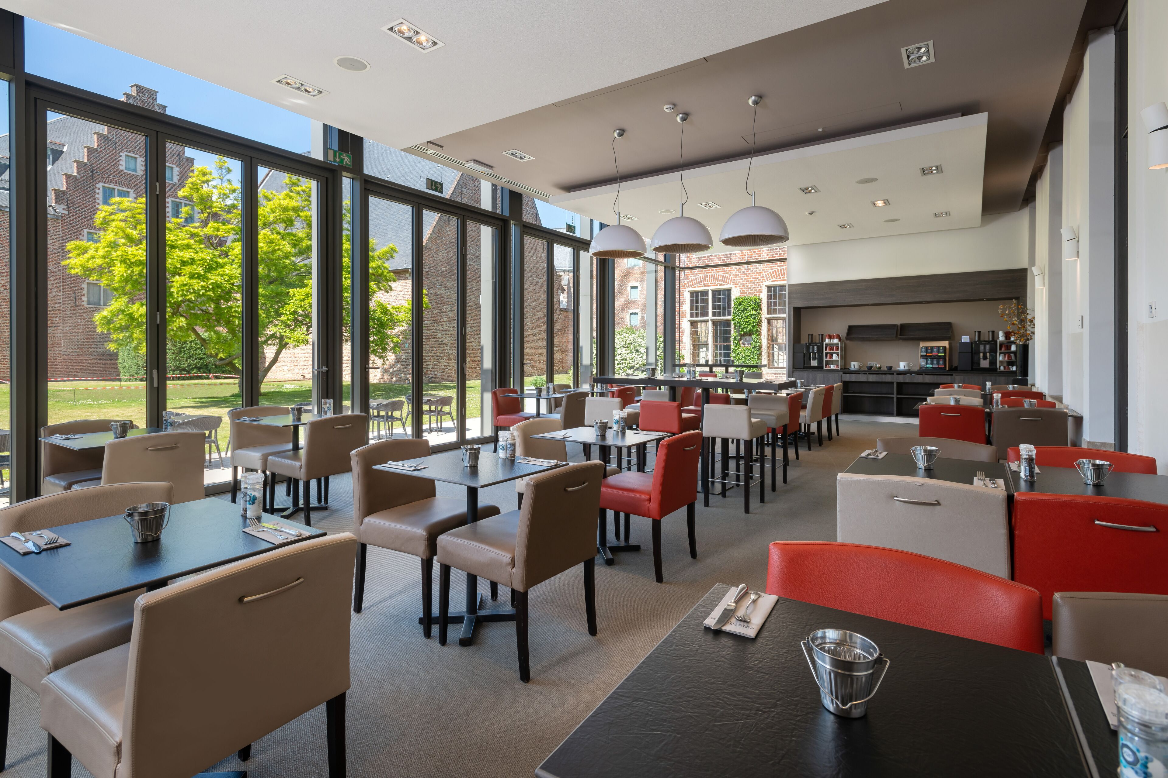 A modern dining area with tables and chairs, large windows, and a kitchen in the background.