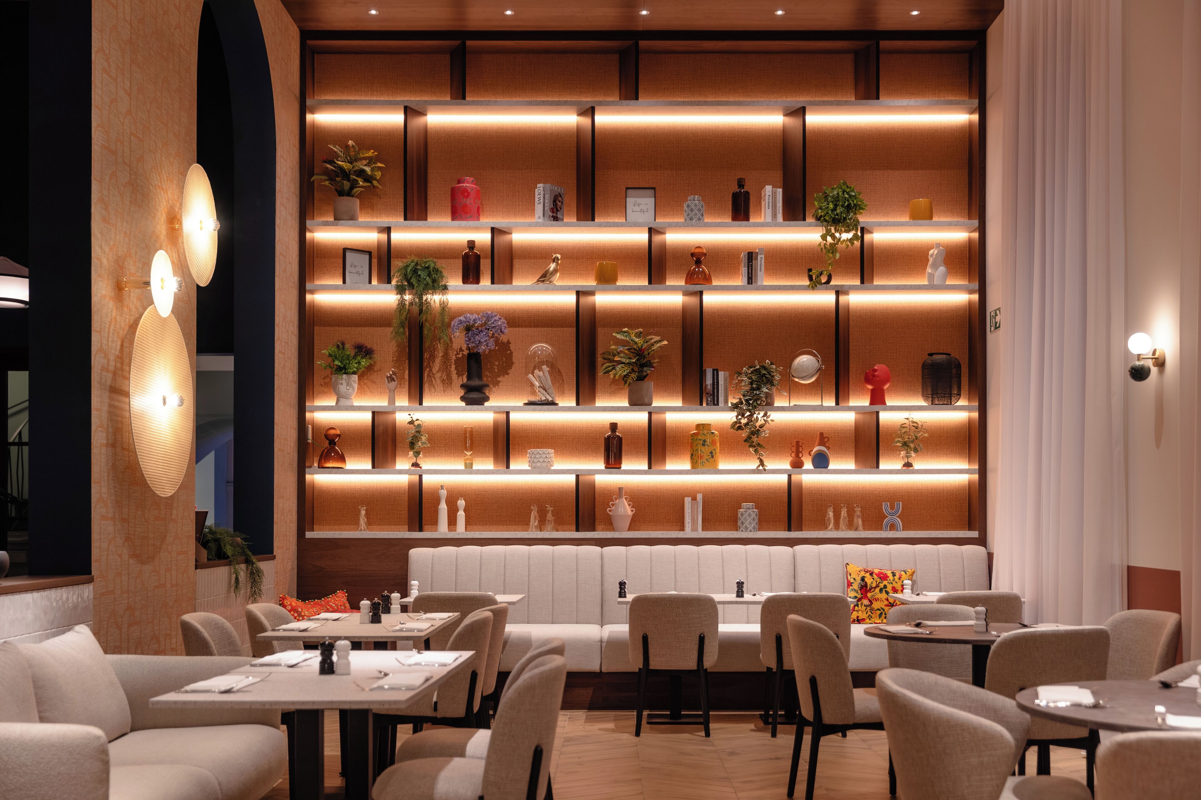 Un restaurant au décor moderne, avec un long comptoir doté de sièges, un éclairage chaleureux et une variété d’objets décoratifs disposés sur des étagères.