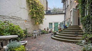 Une cour avec un sol en briques, des sièges extérieurs et des marches menant à l’entrée d’un bâtiment.
