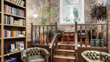 A library with bookshelves, leather chairs, a staircase, and a window with a view.