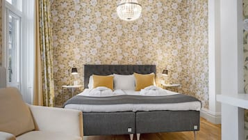 A bedroom with a bed, bedside tables, a chandelier, and floral wallpaper.