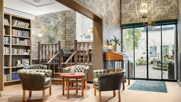 Une bibliothèque avec des fauteuils en cuir, une table en bois et une étagère remplie de livres.