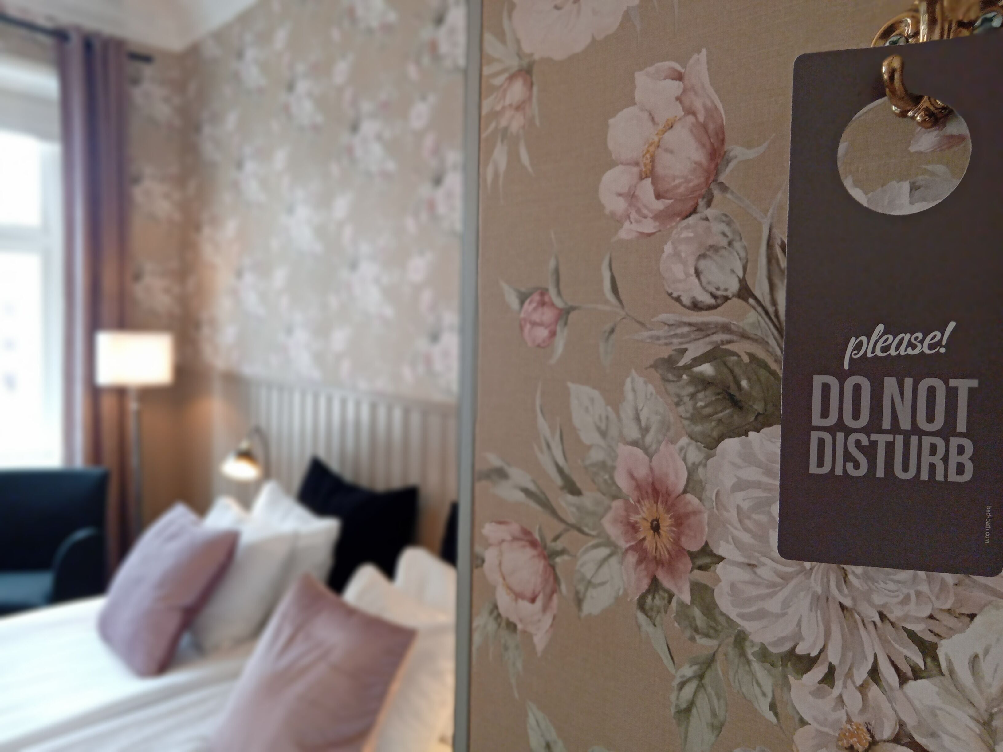 Una habitación de hotel con papel tapiz floral, una cama con varias almohadas y un cartel que dice 'No molestar'.