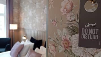 Una habitación de hotel con papel tapiz floral, una cama con varias almohadas y un cartel que dice 'No molestar'.