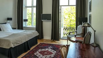 A bedroom with a bed, a desk, a chair, a TV, and a view of greenery through the window.