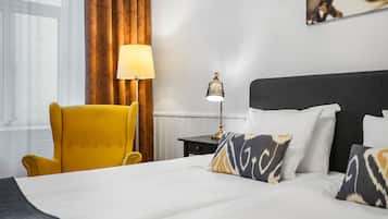 Una camera d'albergo con un letto, una poltrona gialla, un comodino con una lampada e un quadro appeso al muro.