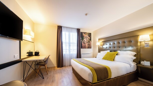 Una habitación de hotel con cama, mesita de noche, lámpara, escritorio con silla y televisión.