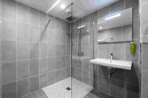 Un baño moderno con ducha envuelta en vidrio, un lavabo blanco y un espejo grande.