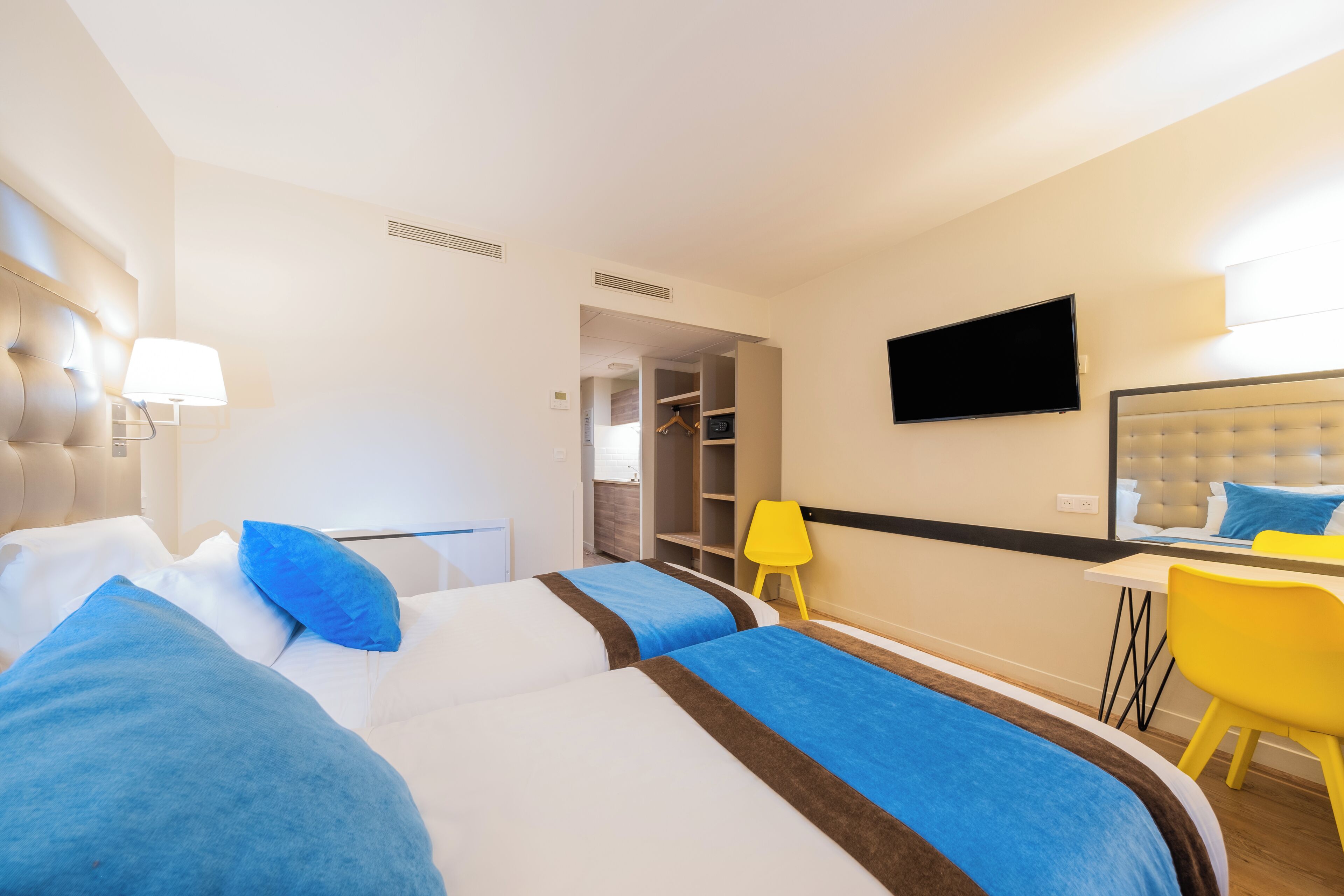 Une chambre d’hôtel avec deux lits, un bureau, une chaise, une télévision et une armoire.